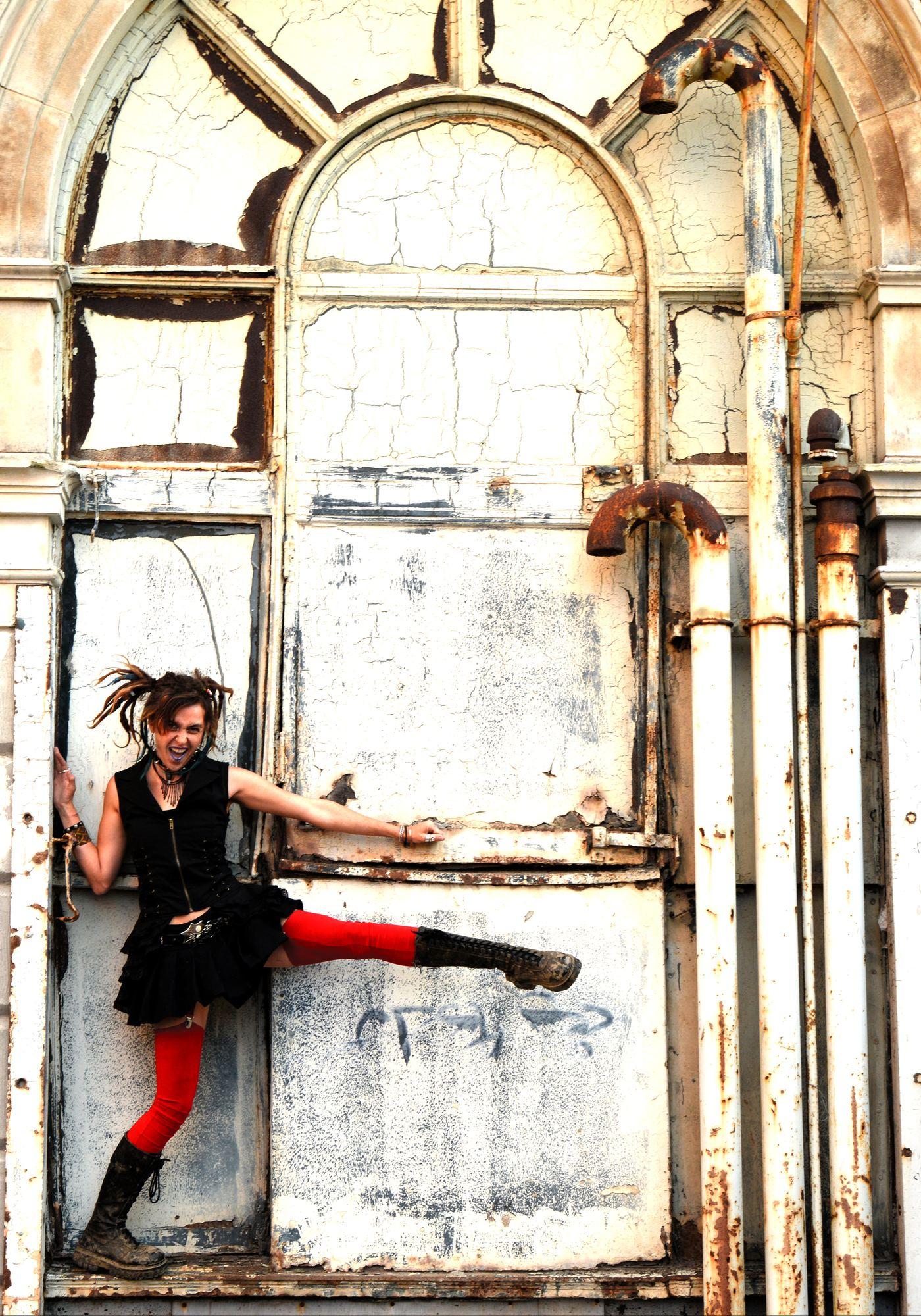 Mad Girl: model in a black ruffled dress and red tights kicking beside a cracked arched doorway
